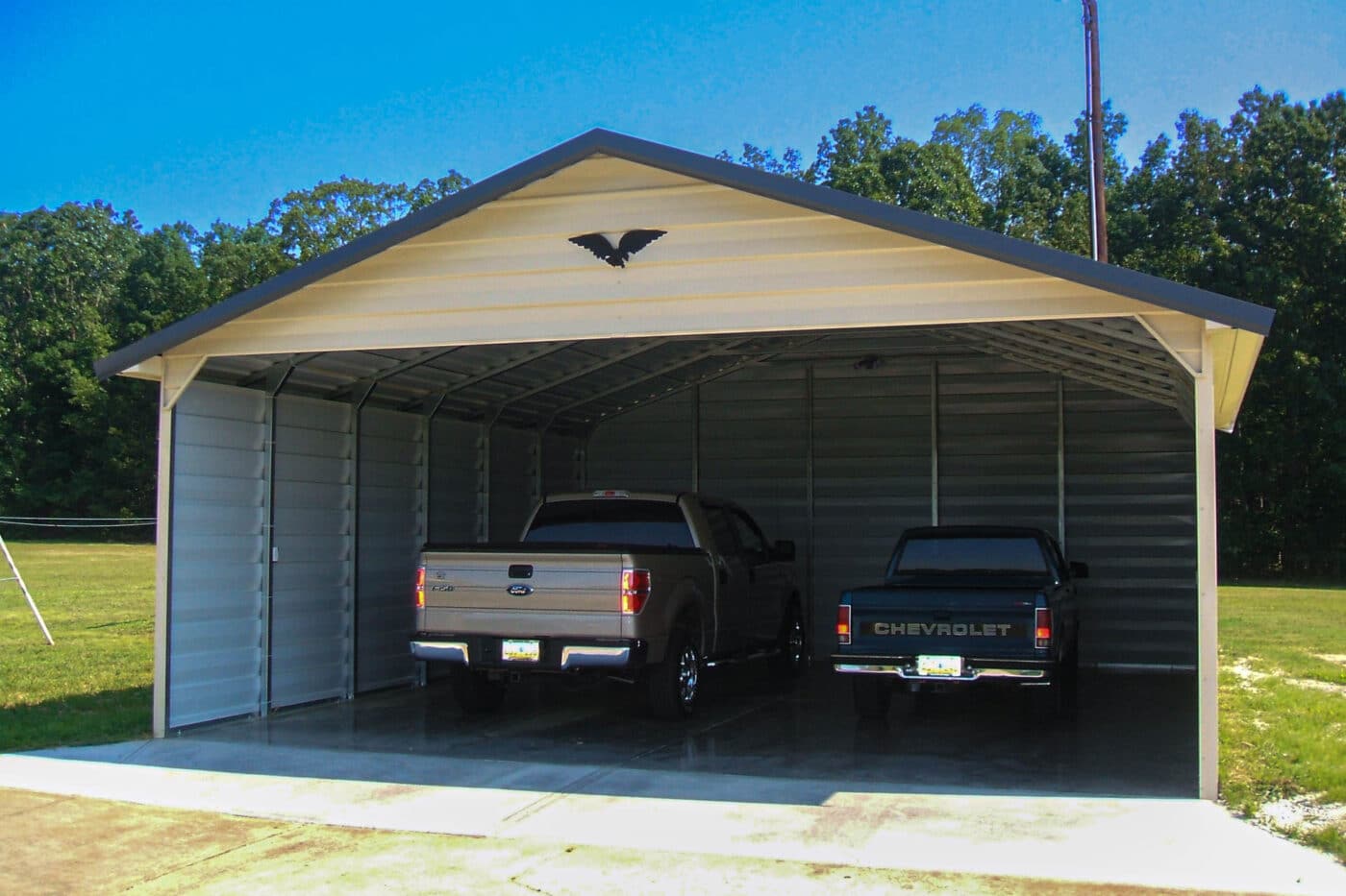 a white 2 car 3 sided enclosed carport cover with a gable roof. includes two trucks parked underneath.