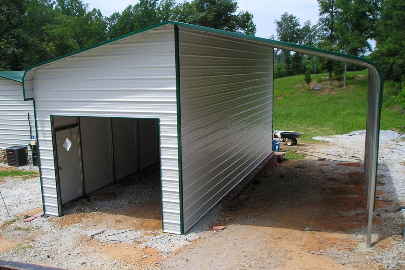 A custom extra tall custom white RV carport cover with attached garage. a green roof and trim finish line the building.