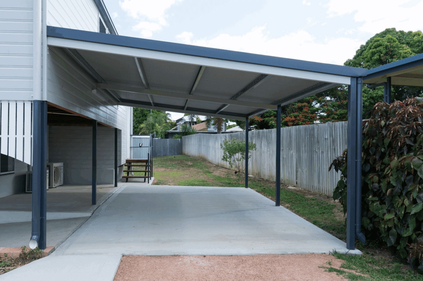a dark grey lean to carport installed on a concrete pad attached to a house